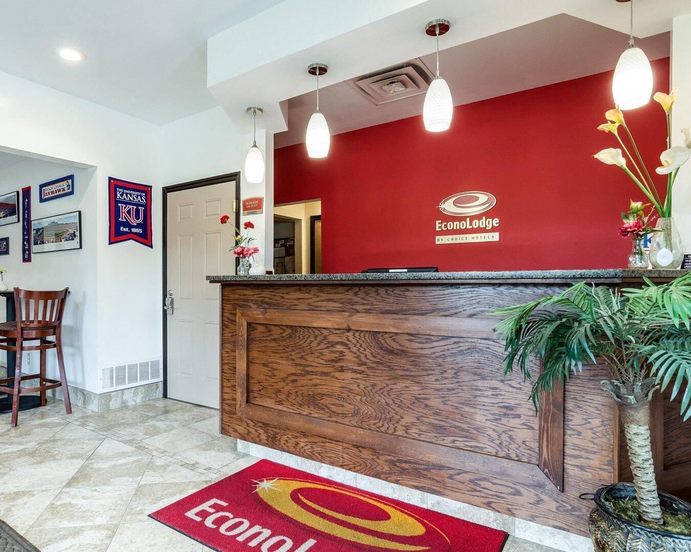 Un comptoir d’accueil avec un mur rouge, un lambris en bois et le logo d’EconoLodge. On y voit des tableaux encadrés, une chaise et une plante.