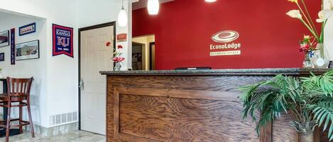 Un comptoir d’accueil avec un mur rouge, un lambris en bois et le logo d’EconoLodge. On y voit des tableaux encadrés, une chaise et une plante.