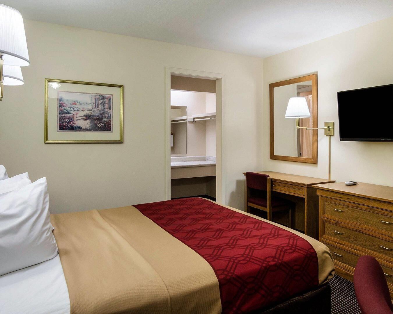 A hotel room with a bed, a desk, a dresser, a television, and a framed picture on the wall.