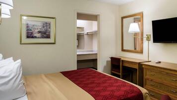 Quarto de hotel com cama, escrivaninha, cômoda, televisão e quadro na parede.