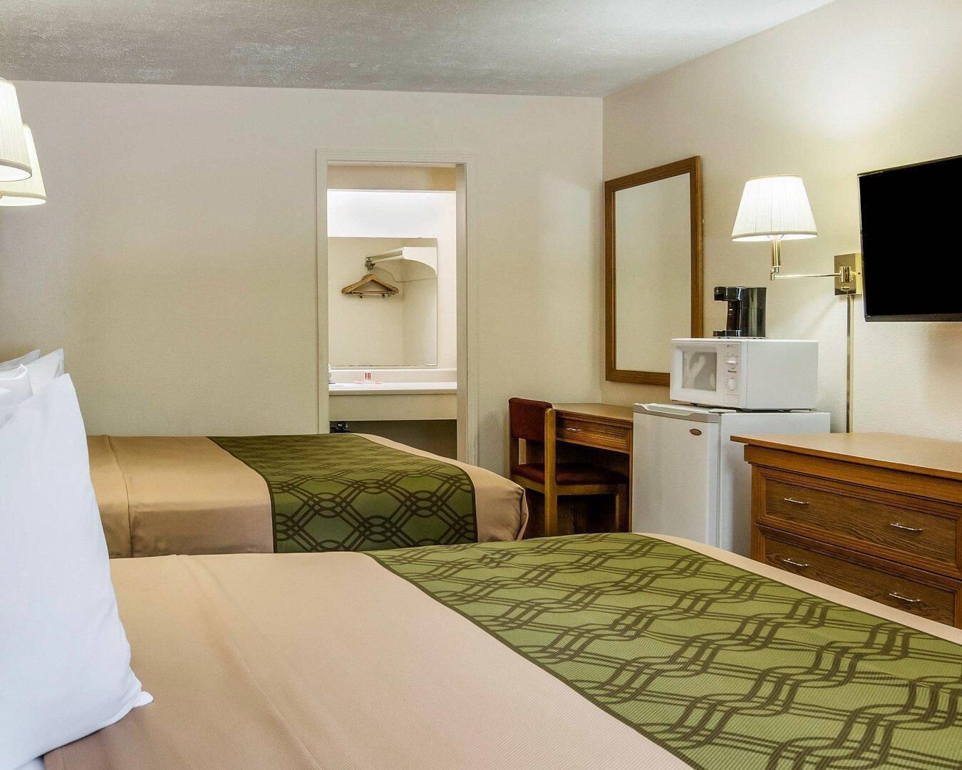 Habitació d'hotel amb dos llits, una taula de treball, una cadira, un microones, un televisor i un armari.