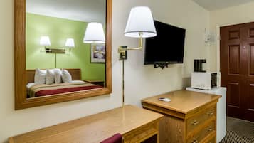 Una habitación de hotel con un escritorio de madera, un espejo, televisor, cafetera y armario.