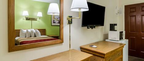 Una habitación de hotel con un escritorio de madera, un espejo, televisor, cafetera y armario.