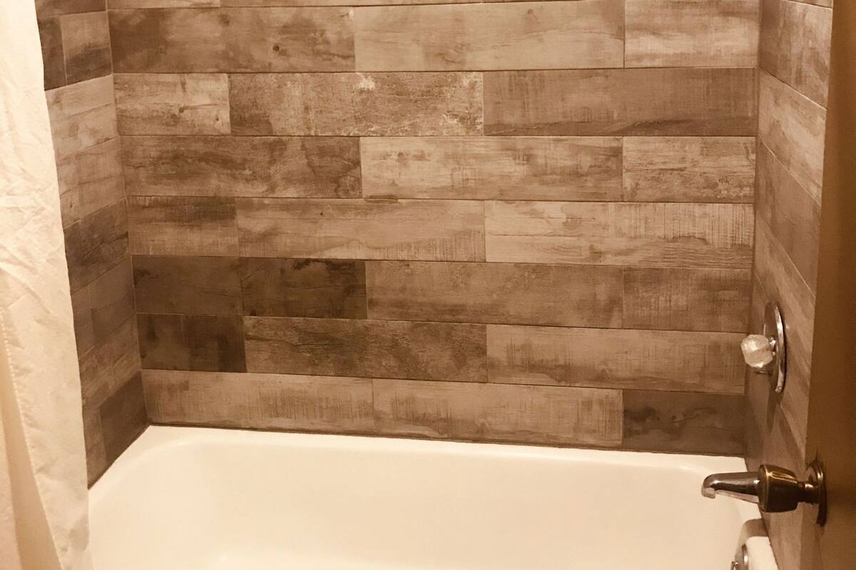 A shower with a tiled wall and a white bathtub.