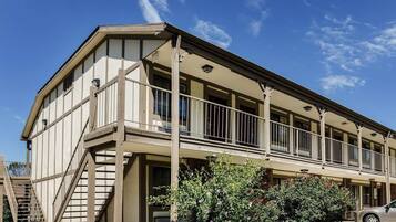 A two-story building with a balcony, a staircase, and a car parked in front.