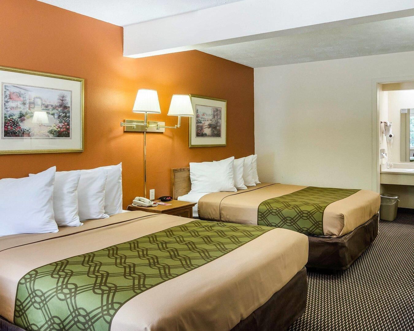 Habitación de hotel con dos camas, una mesita de noche con lámpara, teléfono y un cubo de basura.