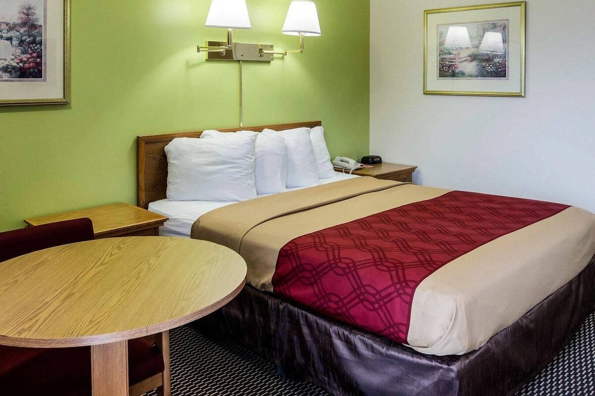 A hotel room with a bed, bedside table, lamp, and a framed picture on the wall.
