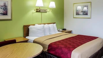 A hotel room with a bed, bedside table, lamp, and a framed picture on the wall.