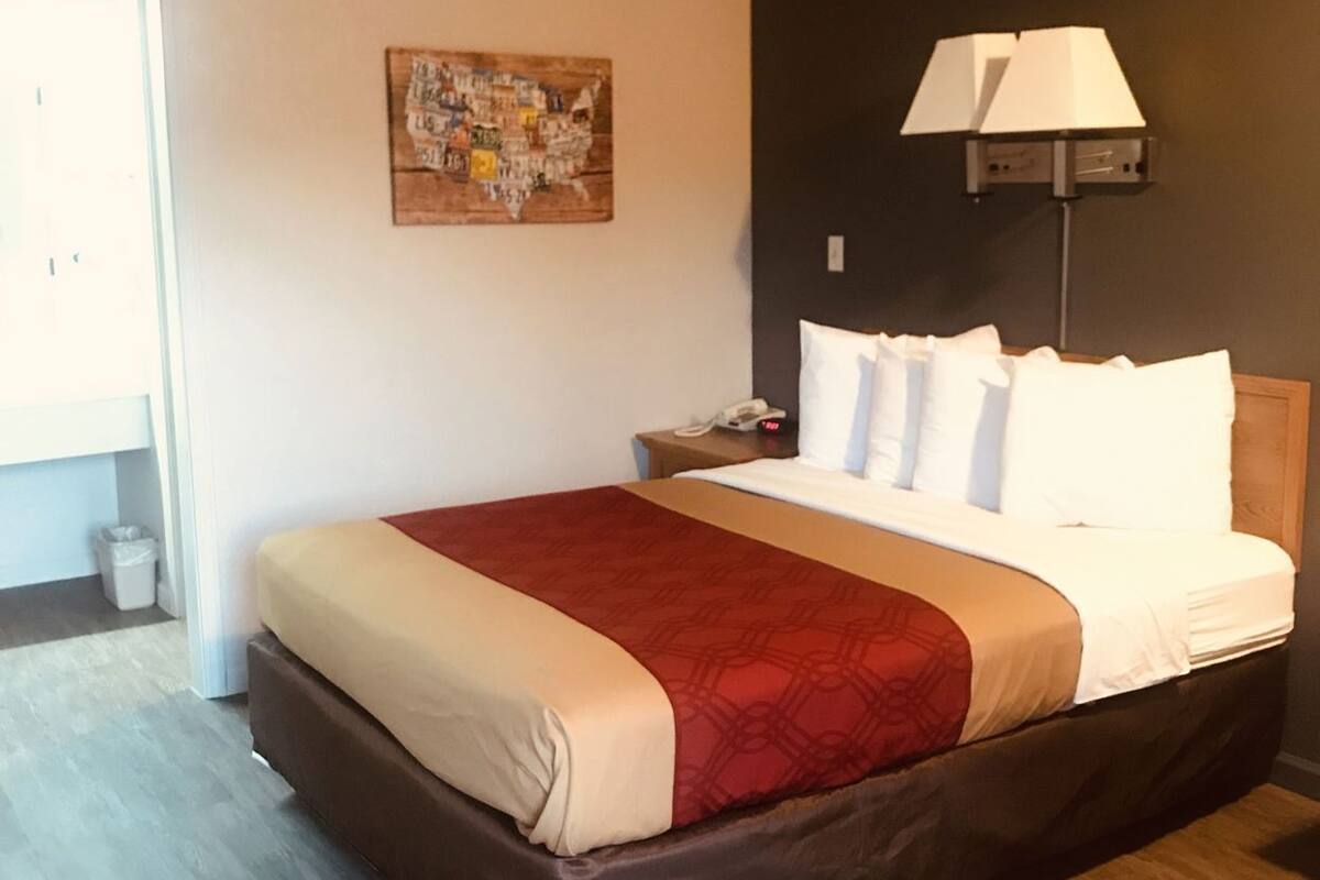 A hotel room with a bed, a nightstand, a lamp, a wall art piece, and a door.