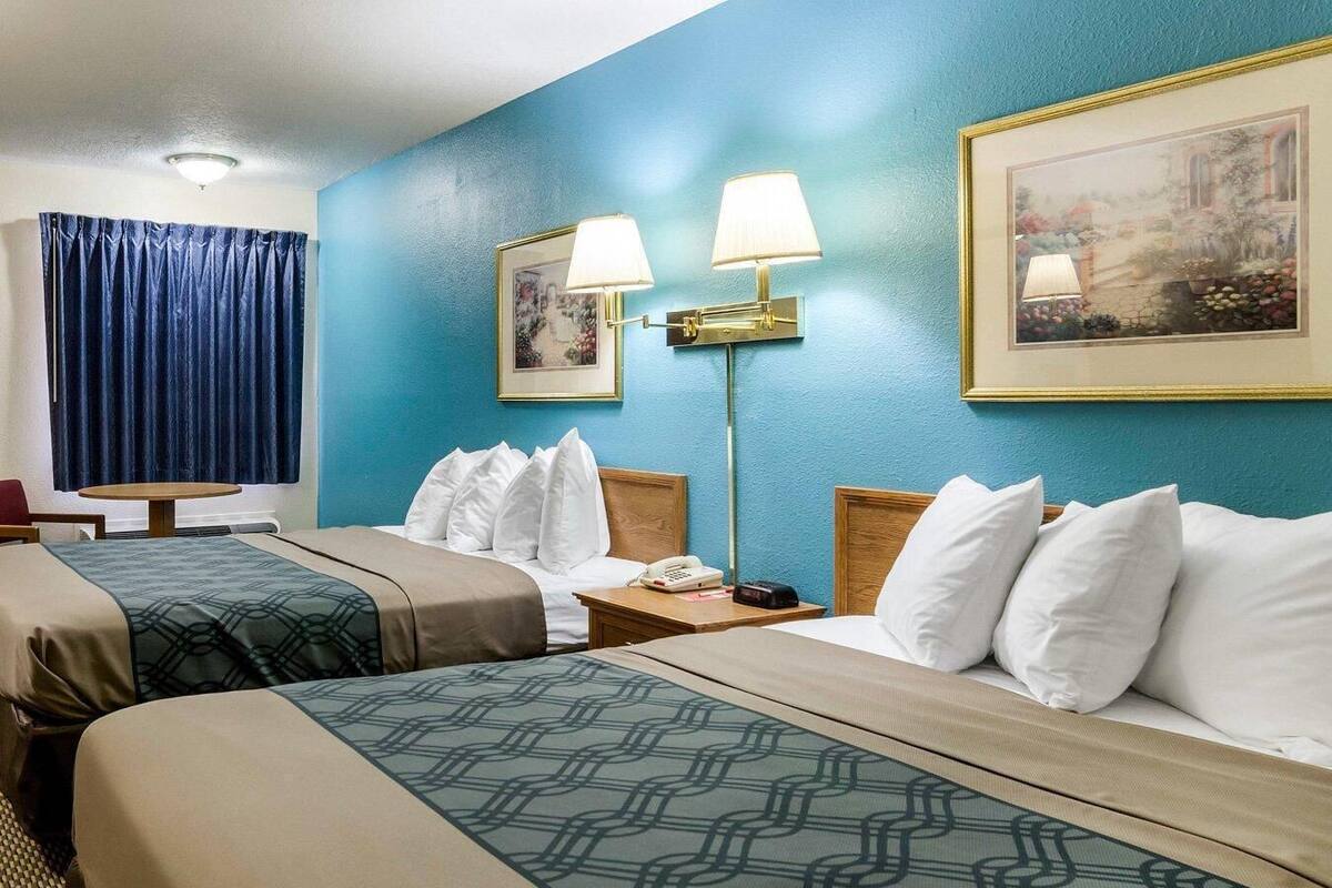 A hotel room with two beds, a desk, a lamp, a telephone, and a painting on the wall.