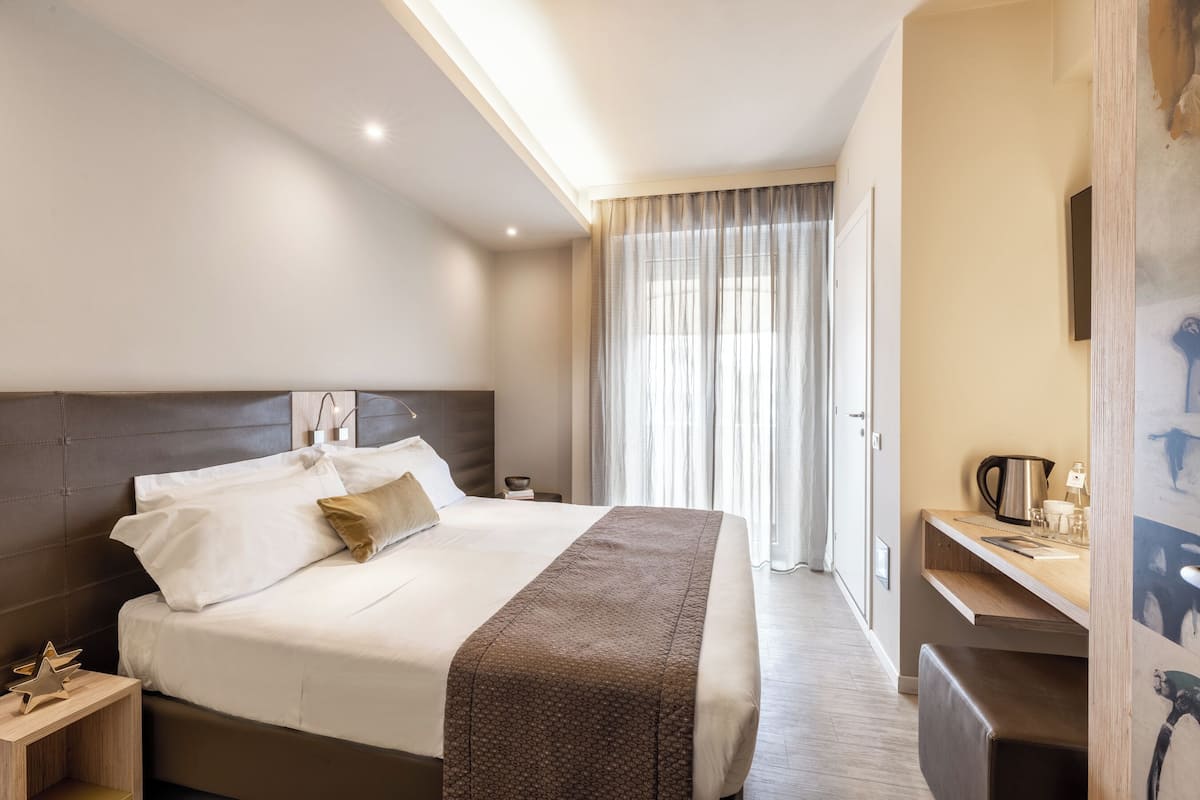 A hotel room with a large bed, bedside tables, a desk, and a window with curtains.
