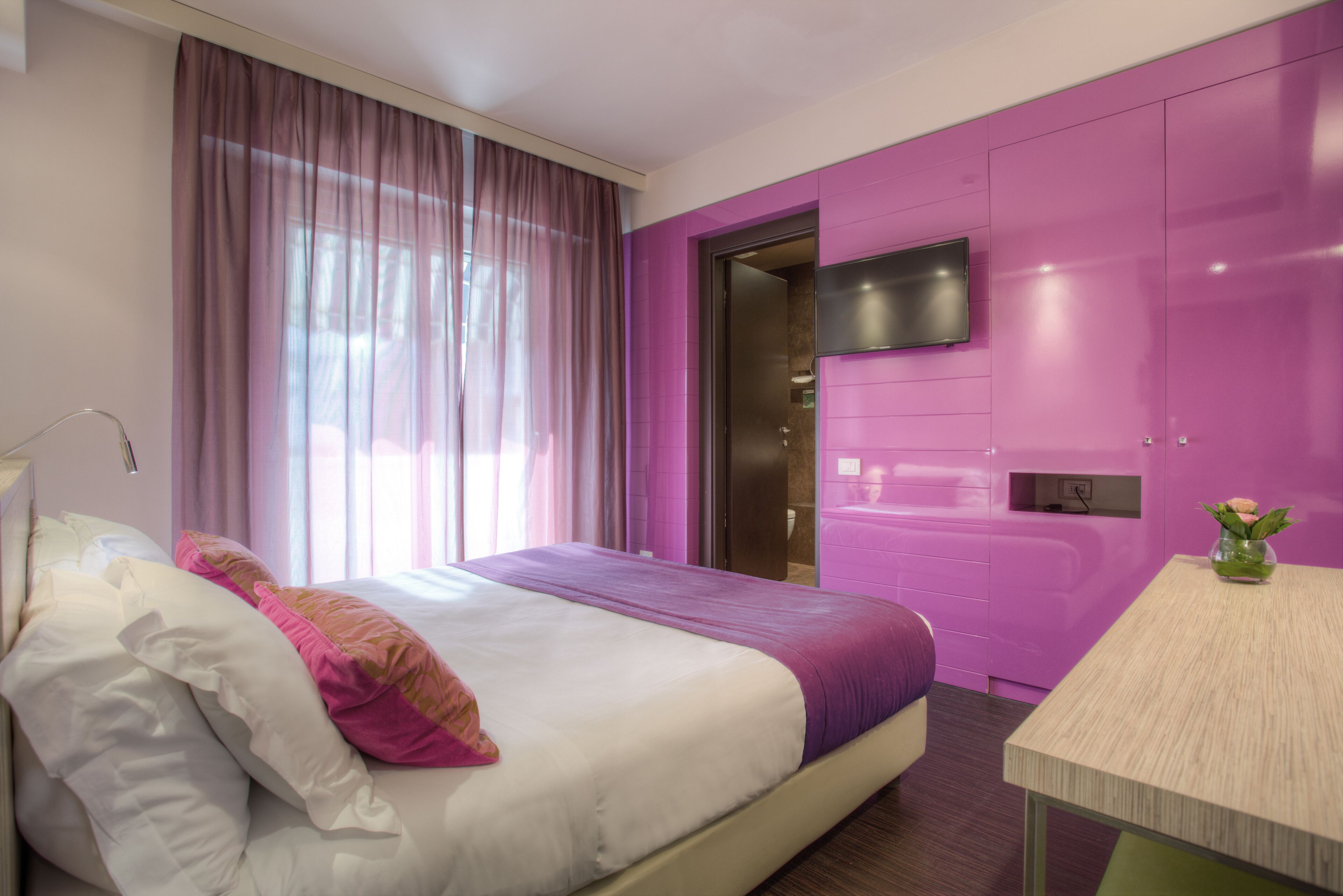 Una habitación de hotel moderna con una cama grande, un escritorio y un baño visible a través de una puerta.