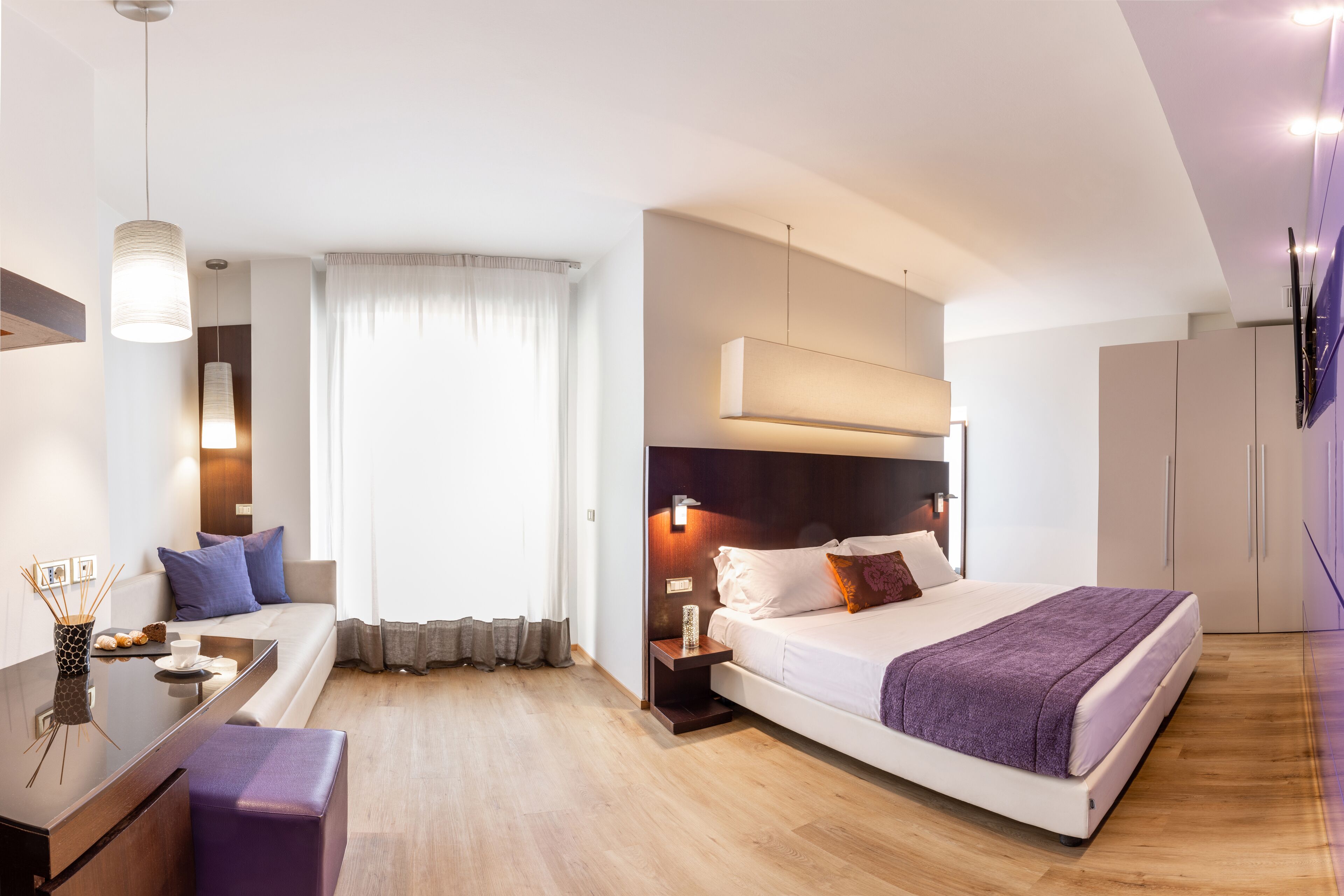 Ein modernes Hotelzimmer mit einem Bett, einer Sitzecke, einem Schreibtisch und einem an der Wand befestigten Fernseher.