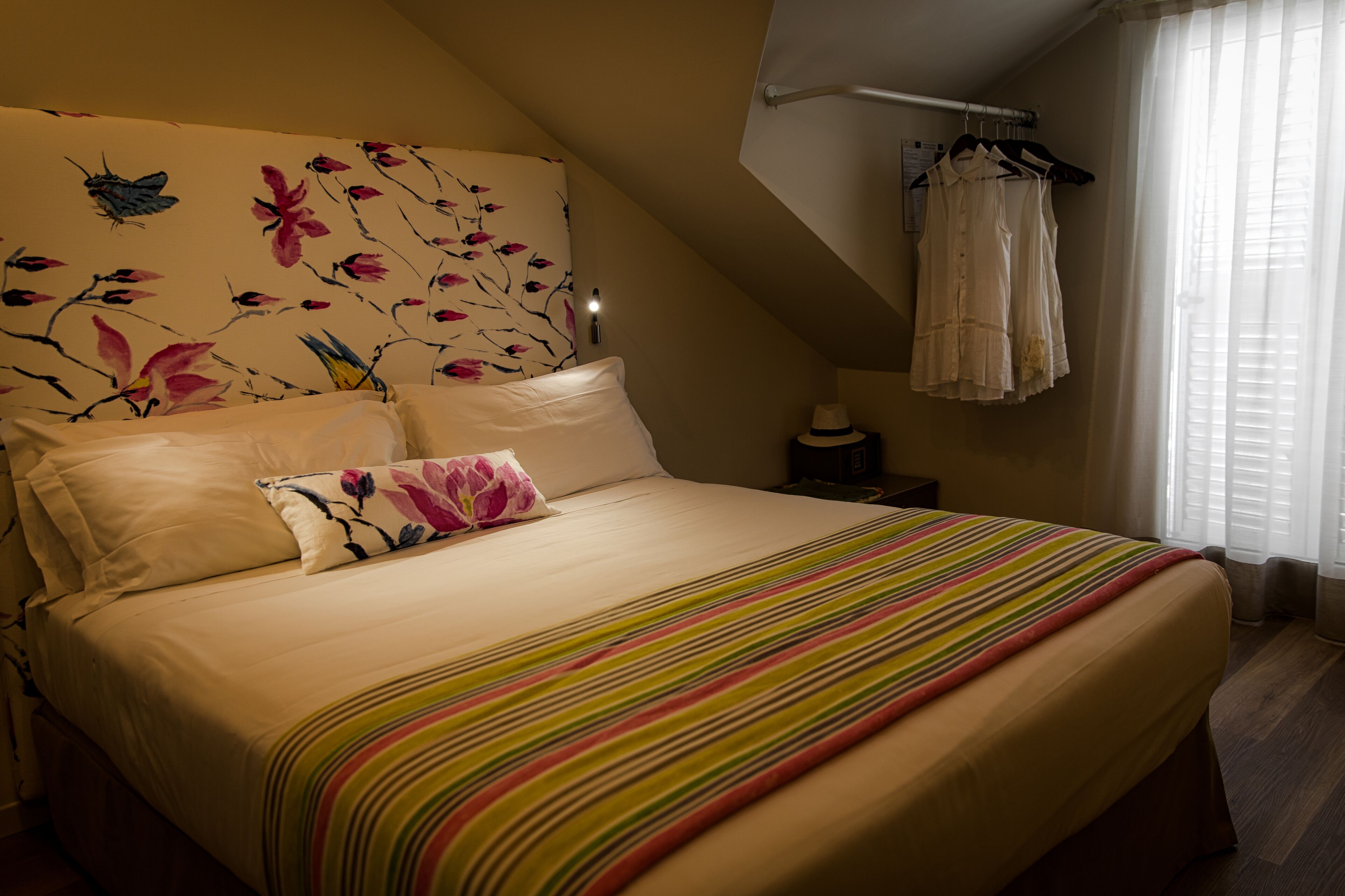 Ein Schlafzimmer mit einem großen Bett, einem blumigen Kopfende und einem Fenster mit Vorhängen.