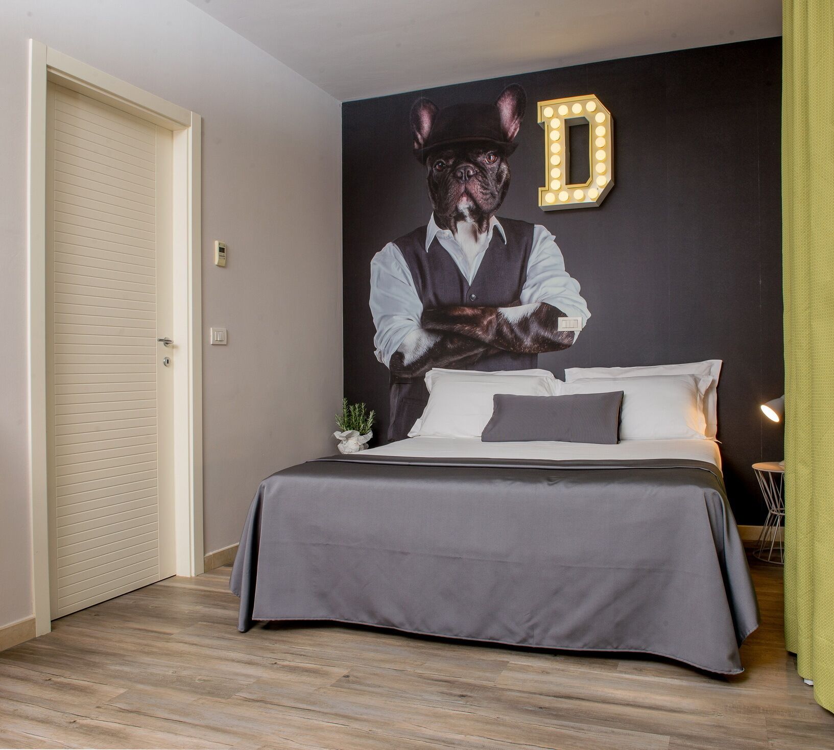 Una camera da letto con un letto, una lampada a parete, una porta e una piccola pianta.