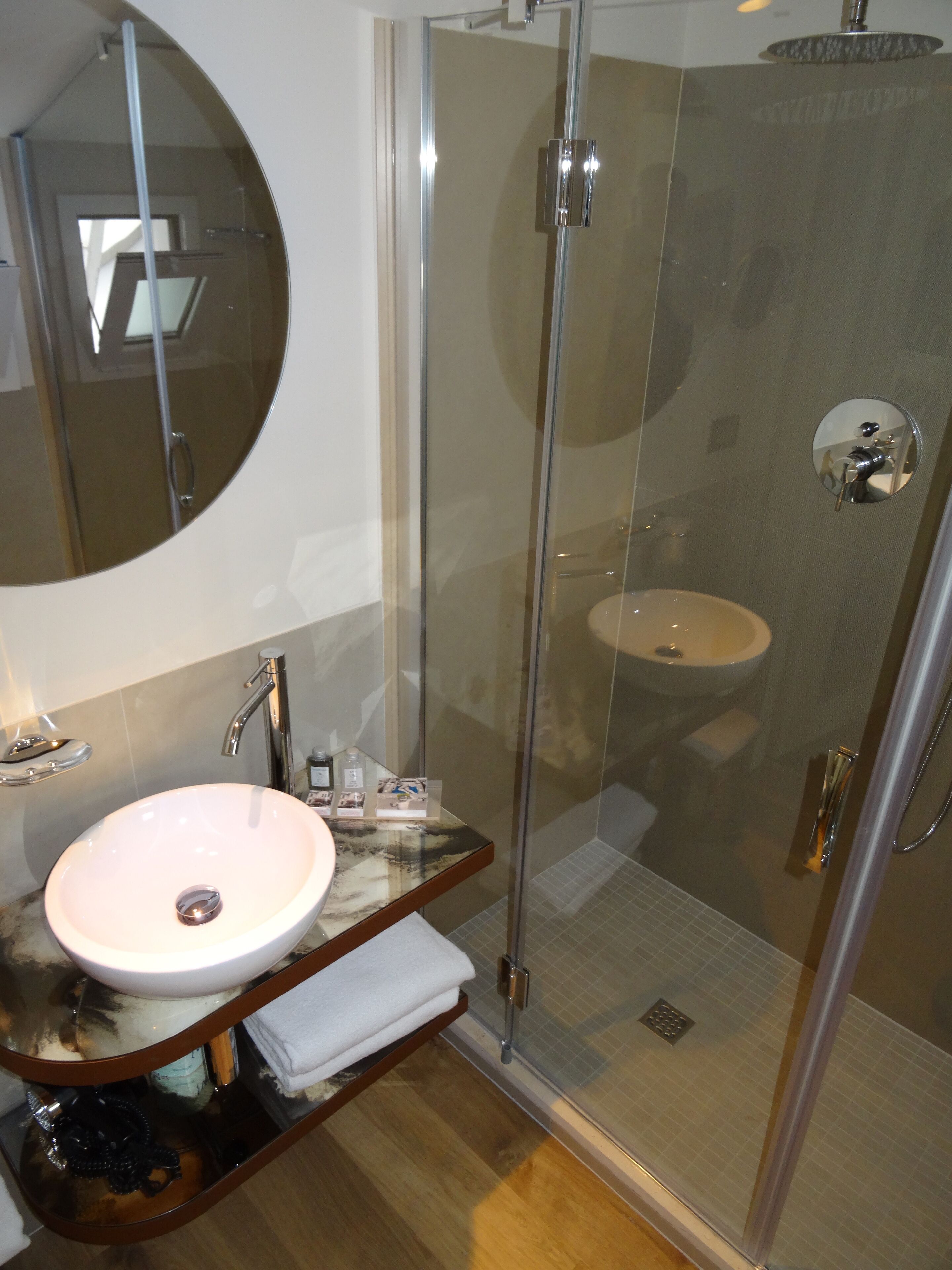 Un baño moderno con ducha envuelta en vidrio, lavamanos de mármol y un espejo grande.