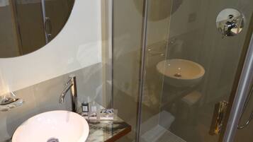 Un baño moderno con ducha envuelta en vidrio, lavamanos de mármol y un espejo grande.