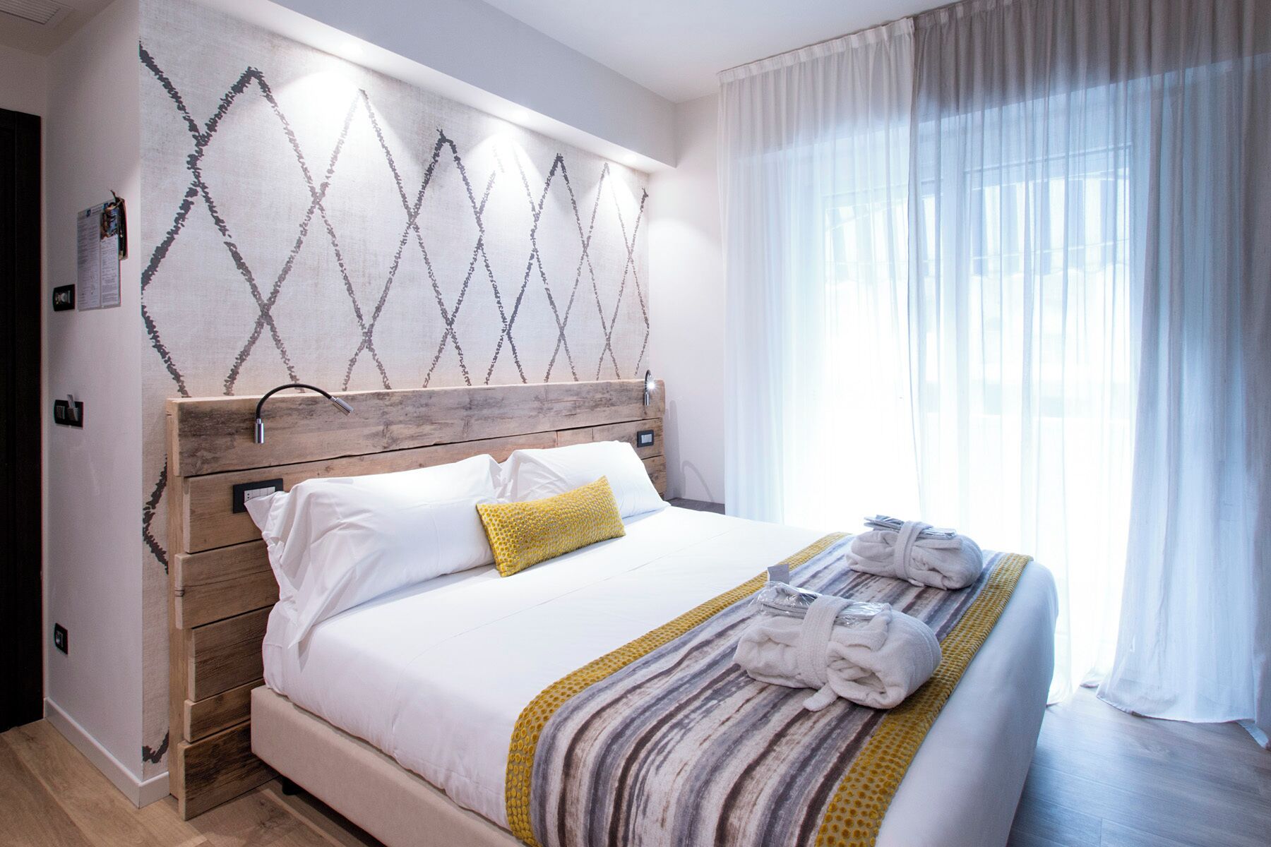 Una cama bien hecha con sábanas blancas, cabecera de madera y una almohada amarilla.