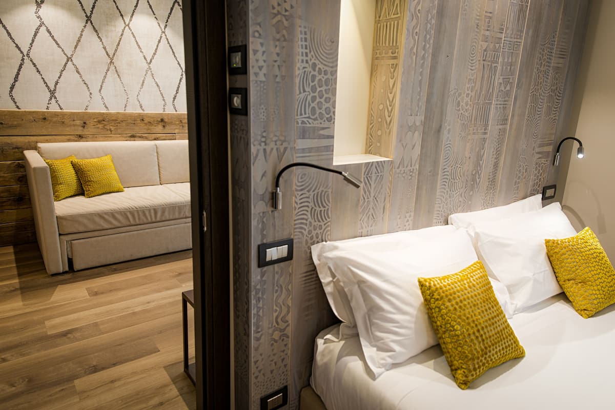 A hotel room with a bed, a sofa, and a wall with patterned wallpaper.