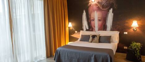 Habitación de hotel con cama, cortinas, lámparas fijadas a la pared y una planta en maceta.