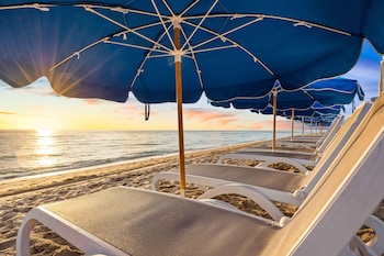 A poolside area with wooden tables and chairs, a glass barrier, and a view of the ocean at sunset. at Marenas Beach Resort