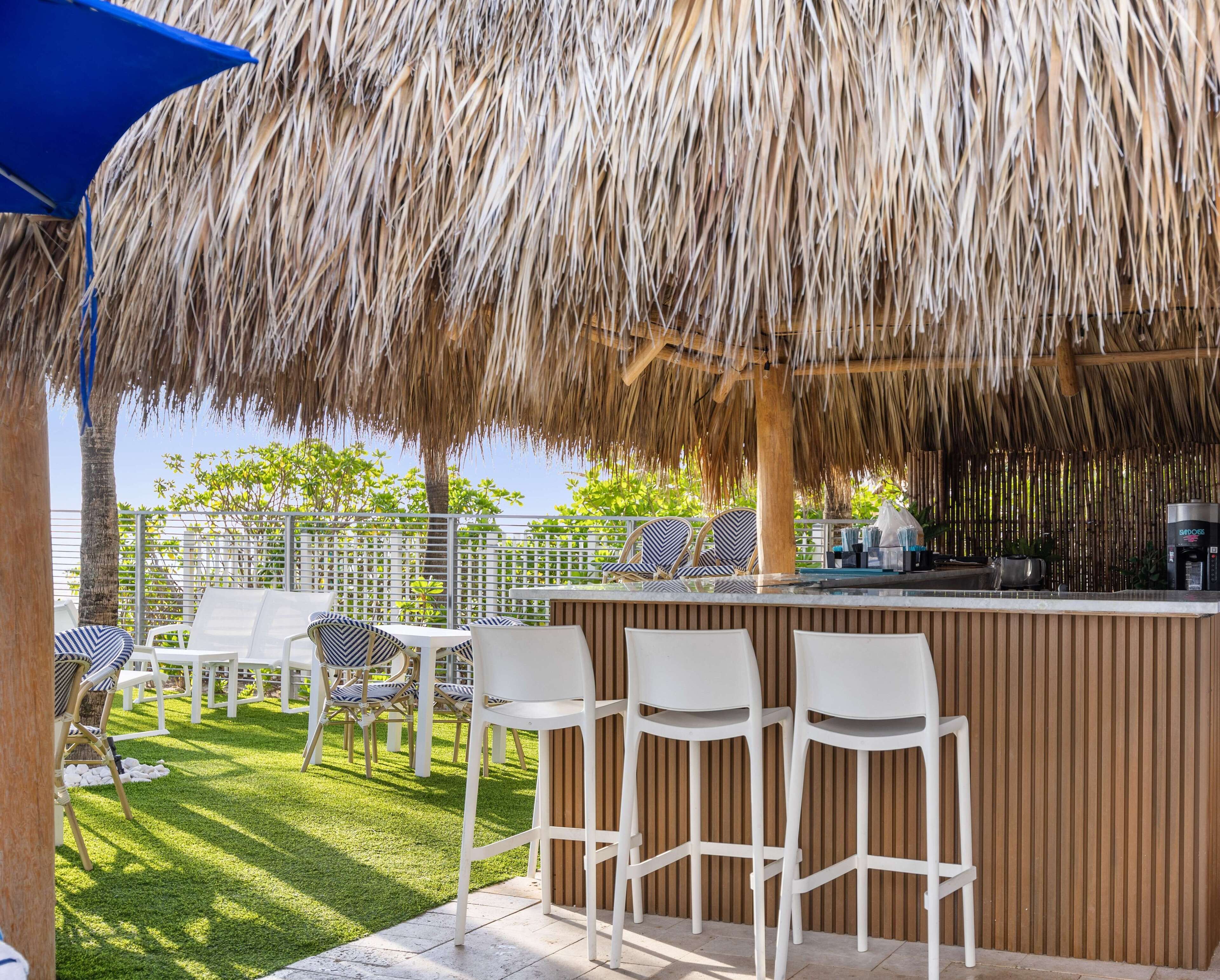 Een overdekt terras met rieten dak, witte barstoelen en een bargedeelte.