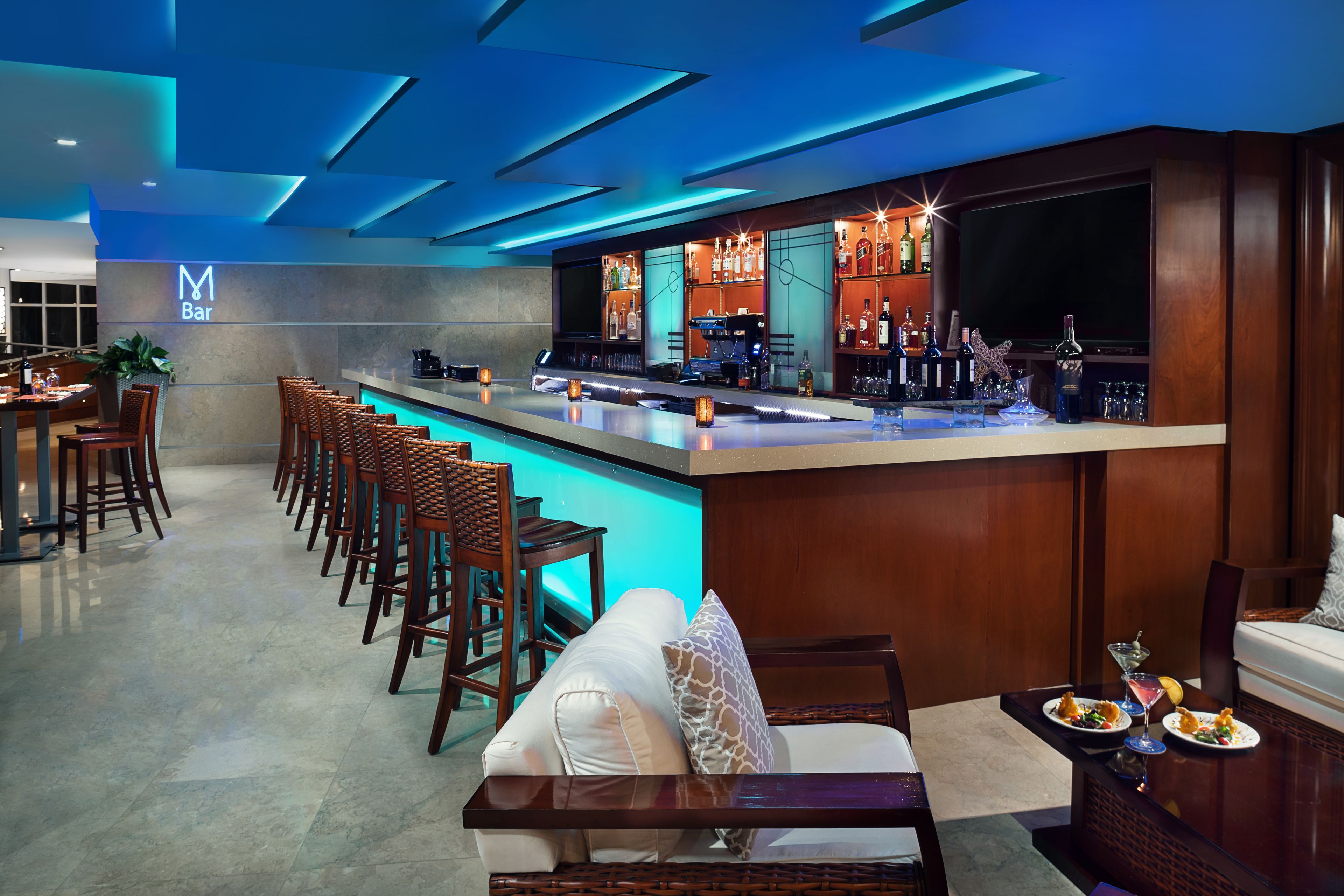 Un bar moderno con una barra larga, taburetes y un área de estar con un sofá y sillas.