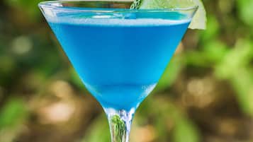 Un cóctel azul en una copa de martini con una cuña de lima en el borde, sobre una mesa tejida.