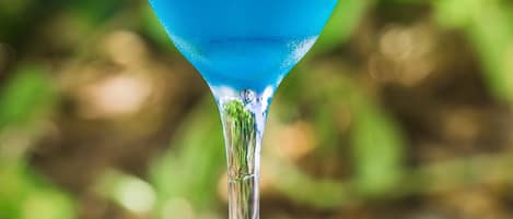 A blue cocktail in a martini glass with a lime wedge on the rim, placed on a woven table.