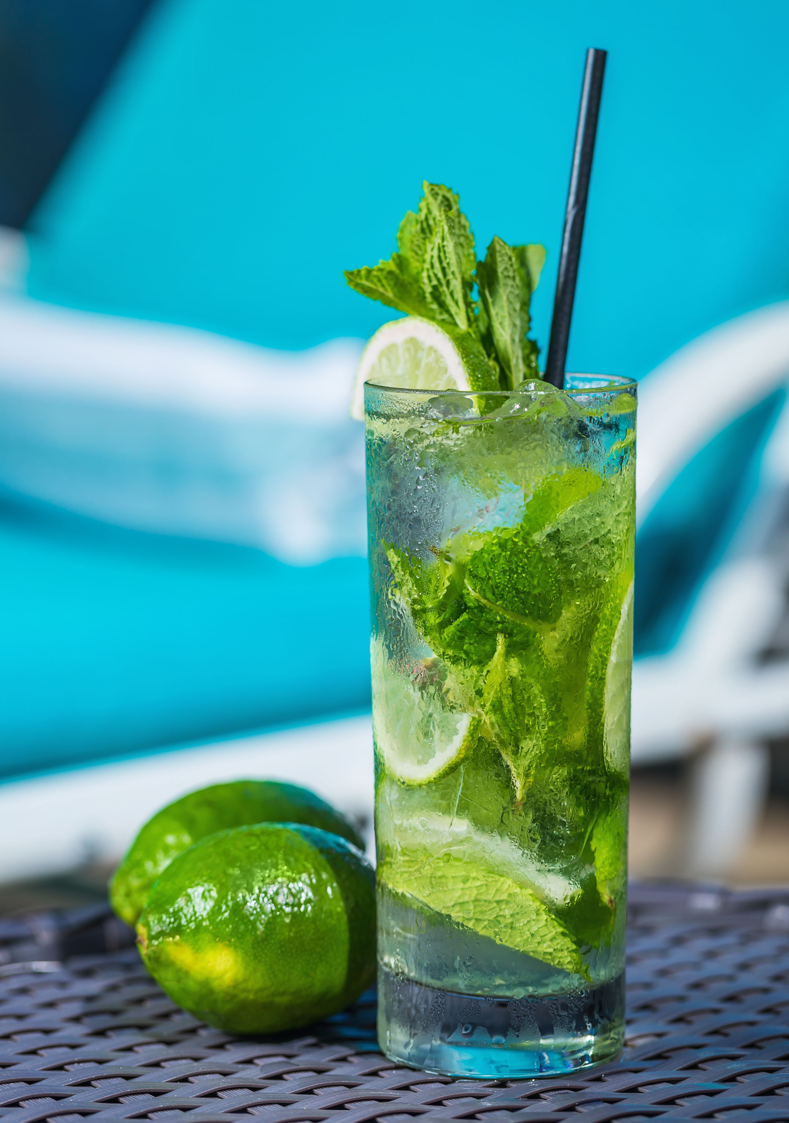 A tall glass of a refreshing drink with lime and mint, placed on a metal table with a blue background.