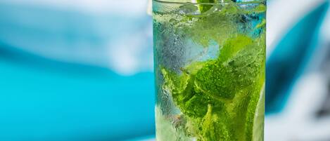 A tall glass of a refreshing drink with lime and mint, placed on a metal table with a blue background.