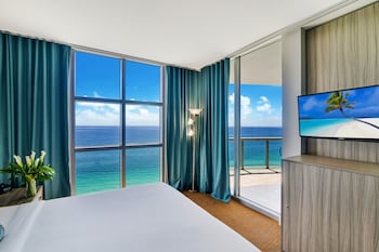 Enjoy ocean views from the large window in this stylish room featuring a comfortable bed, flat-screen TV, and elegant nightstand. at Marenas Beach Resort