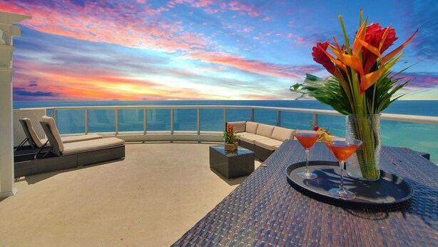 A sunlit balcony with a view of the ocean, a sofa, a small table with drinks, and a vase with flowers. - Marenas Beach Resort (Sunny Isles Beach)