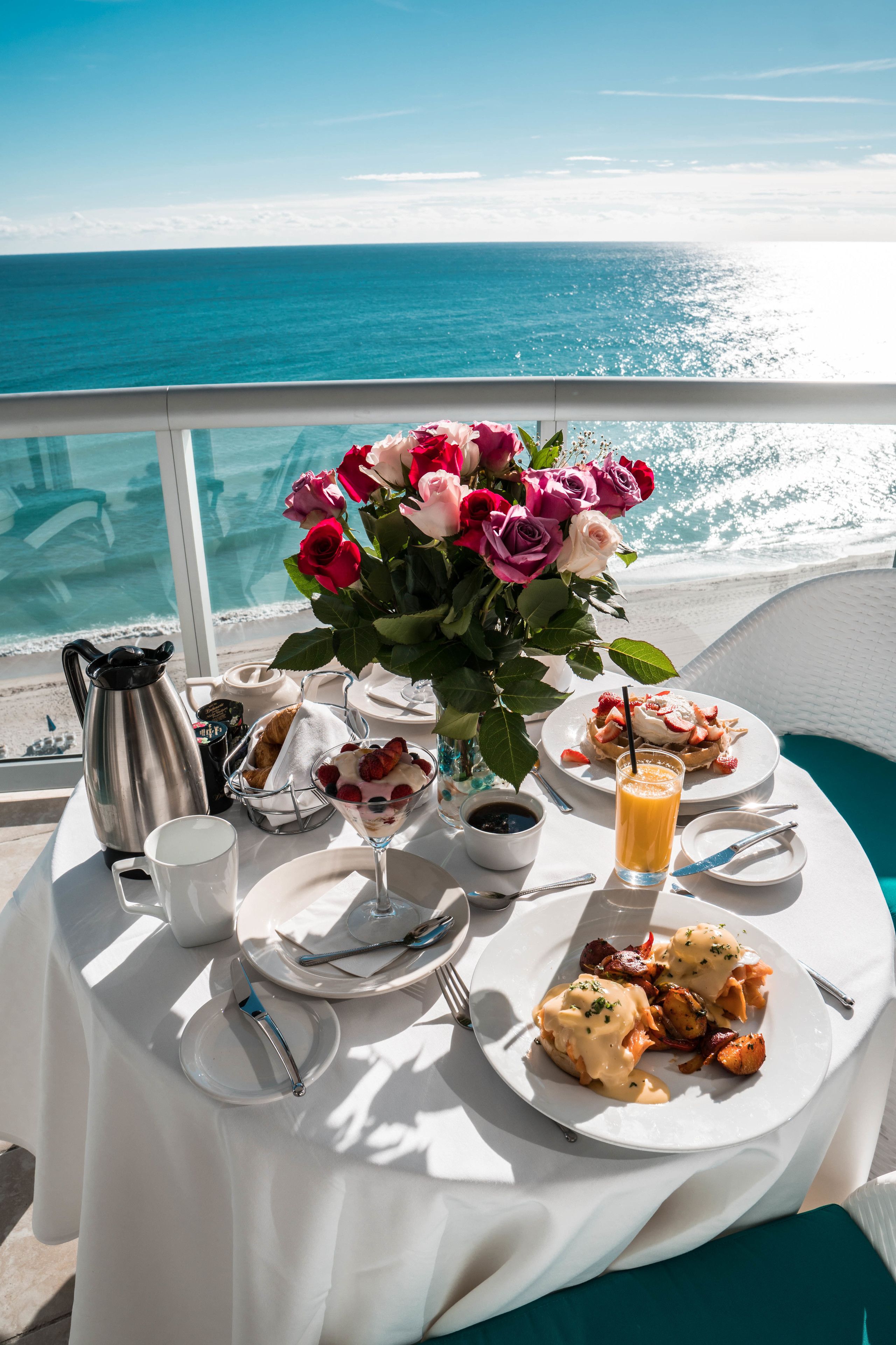 Ett bord dukat med frukostmat, en bukett blommor och utsikt över havet.