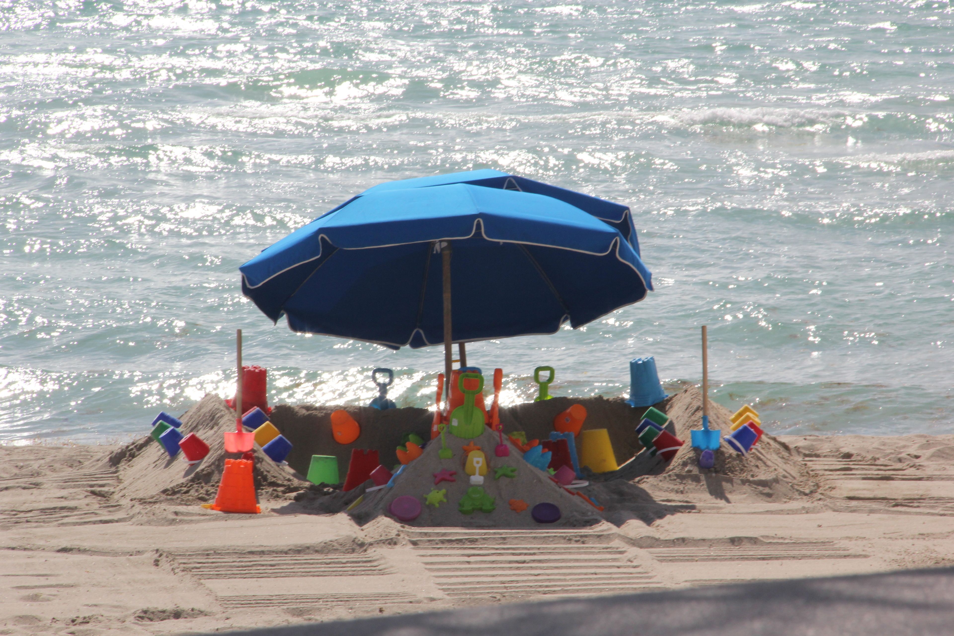Una playa con un paraguas azul y juguetes de colores.
