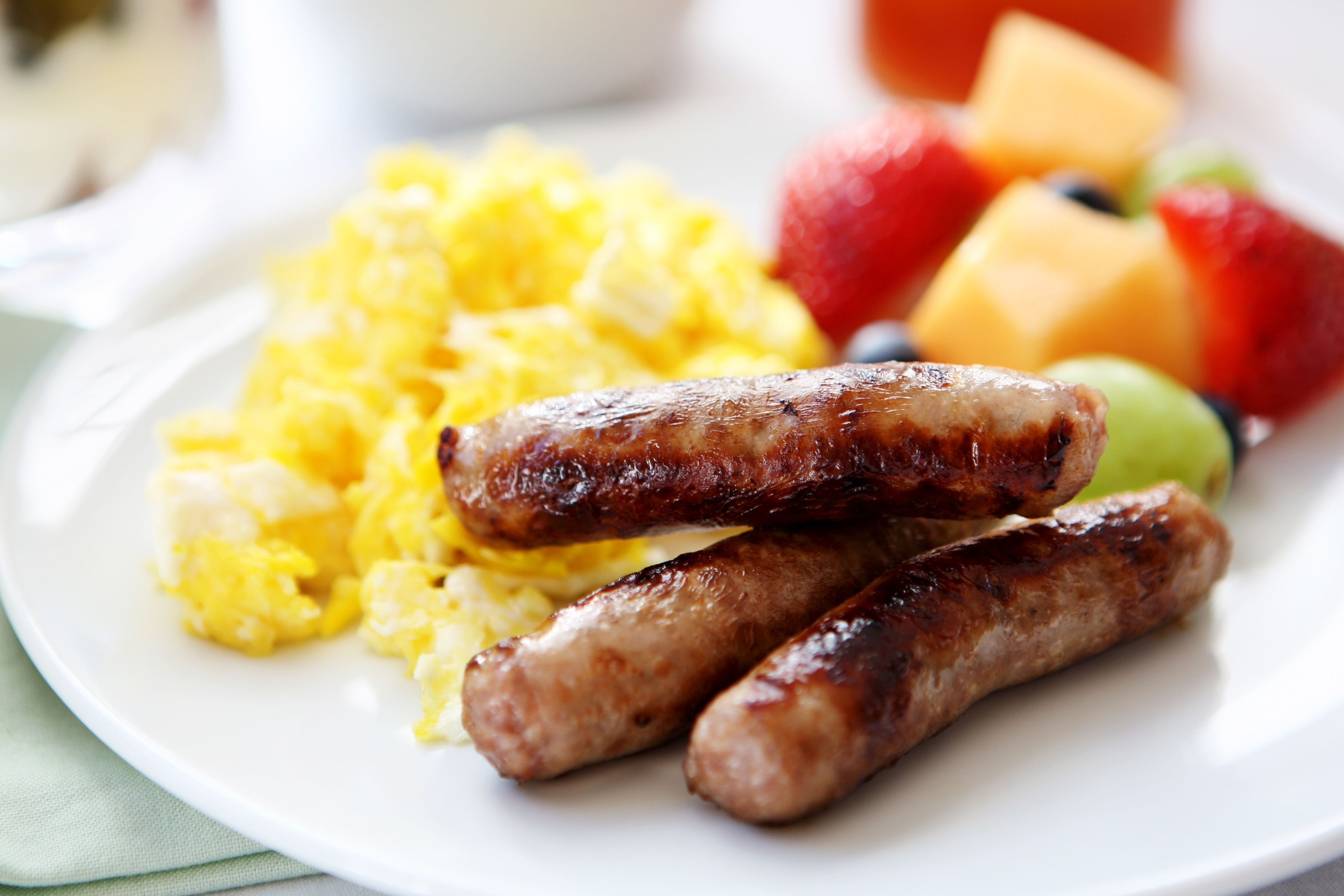 A plate with scrambled eggs, sausages, and fruit.