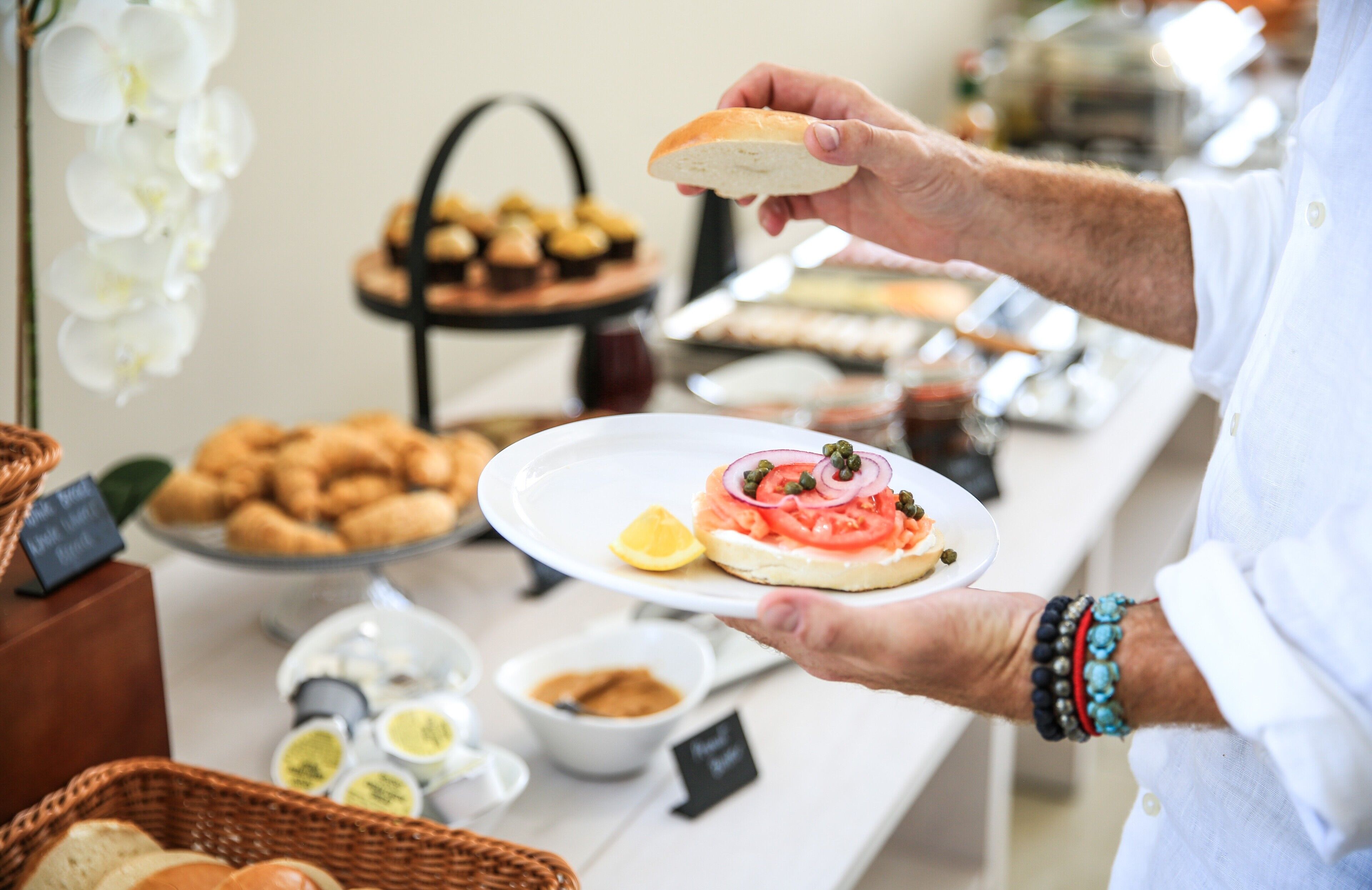 Montaje de bufé con diversas opciones de comida y una persona sirviendo un sándwich.