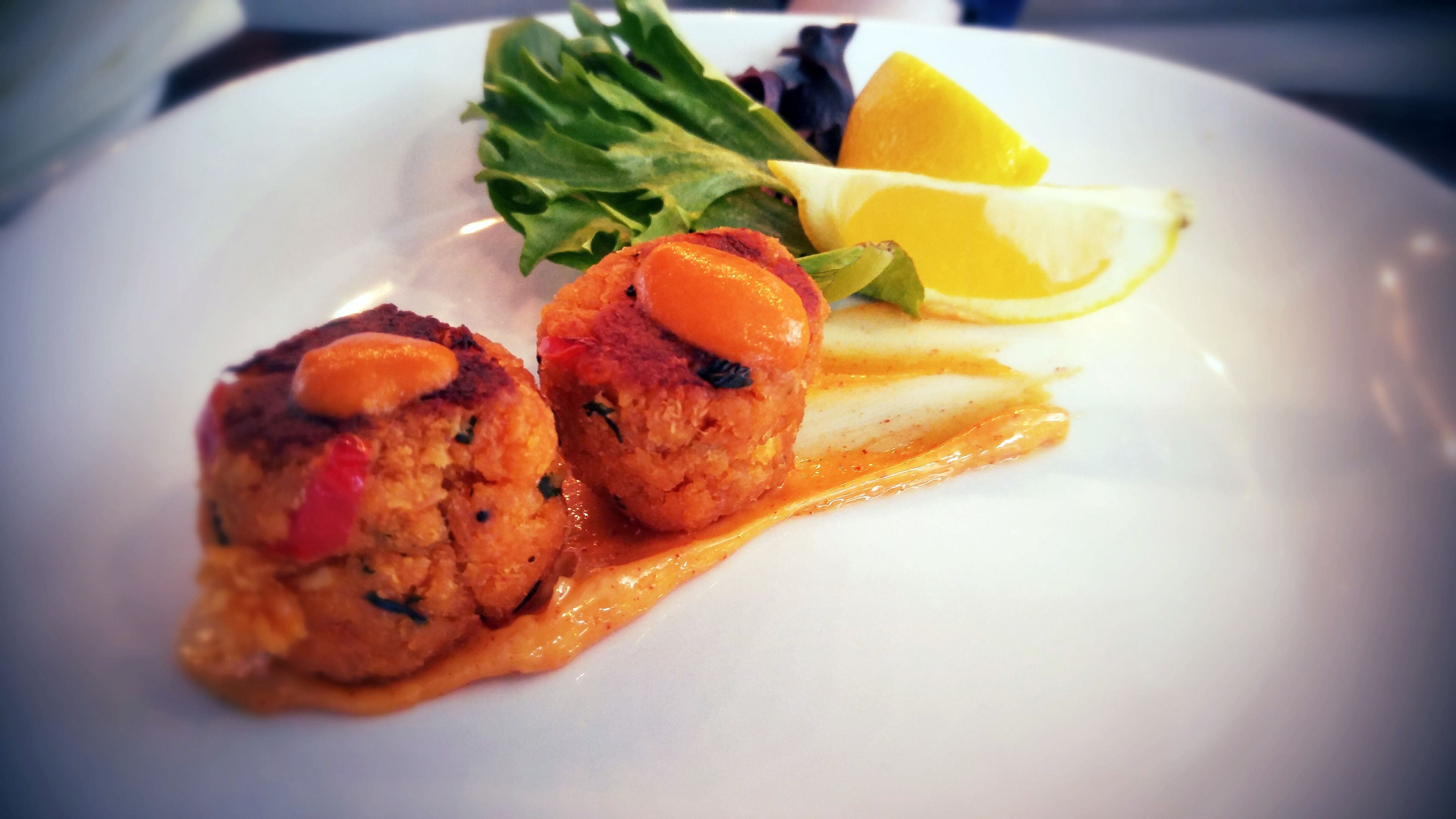 A plate with two crab cakes, lemon slices, and greens.