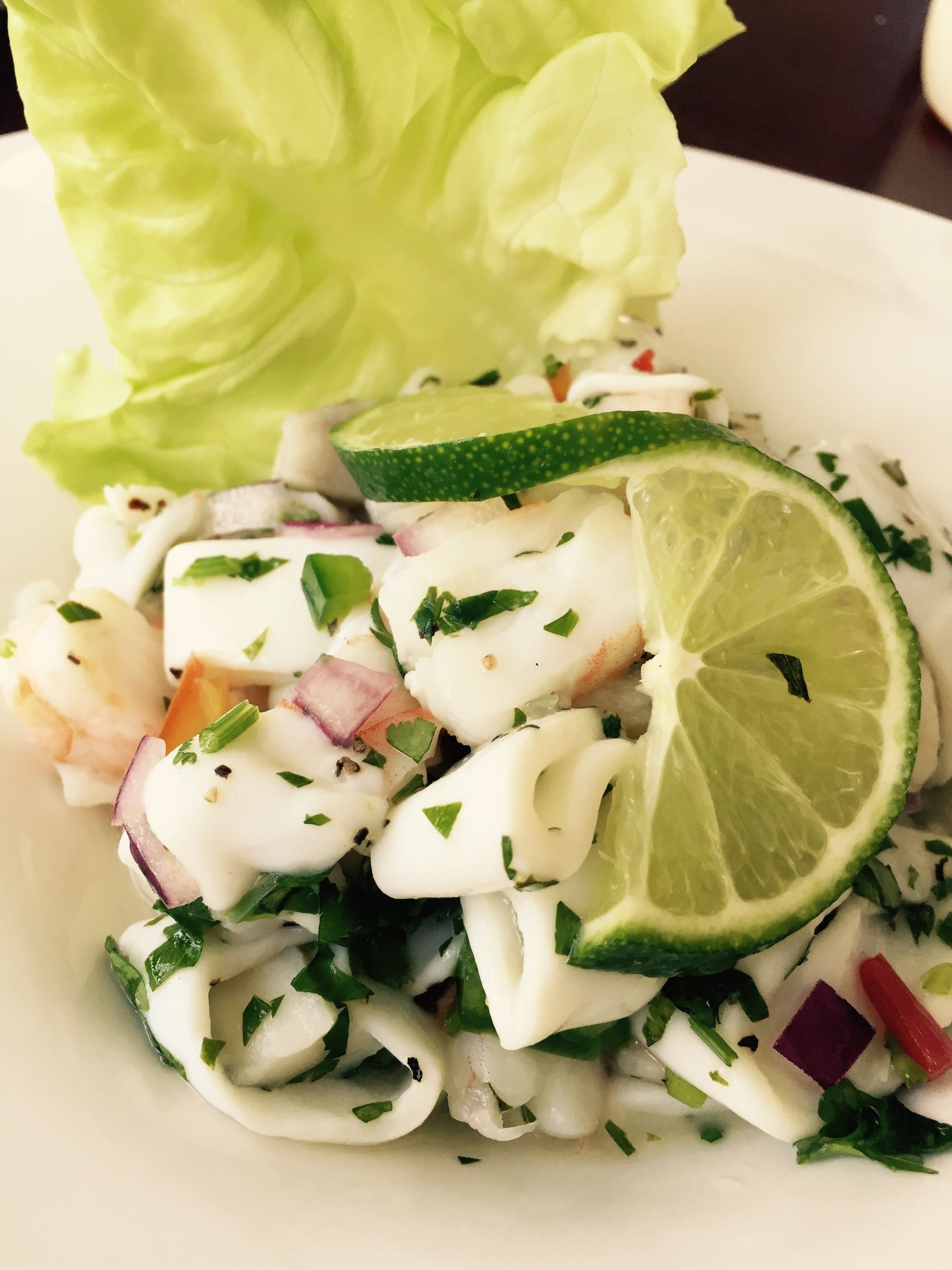 Eine Schale mit Seafoodsalat, darunter Garnelen, Zwiebeln und Kräuter, mit einer Limettenscheibe verziert.
