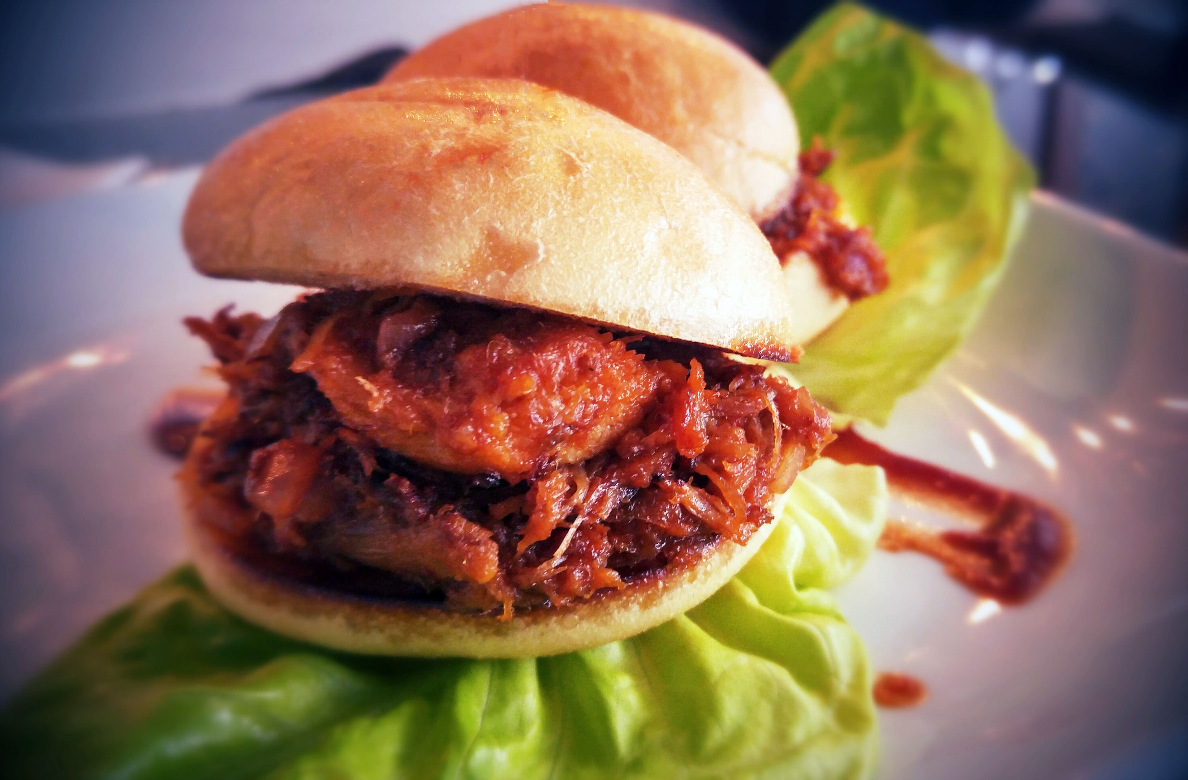 A sandwich with shredded meat and a bun, served on a plate with lettuce.