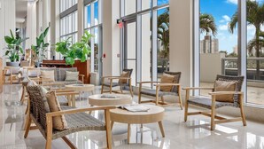 A spacious lobby with large windows, wicker furniture, and potted plants. - Marenas Beach Resort (Sunny Isles Beach)