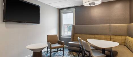 A conference room with a large flat-screen TV, a round table, two chairs, a sofa, and a patterned carpet.