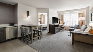 Une chambre d’hôtel dotée d’une kitchenette, d’un coin repas, d’un salon avec un canapé et une télévision, ainsi que d’une grande fenêtre avec des rideaux.
