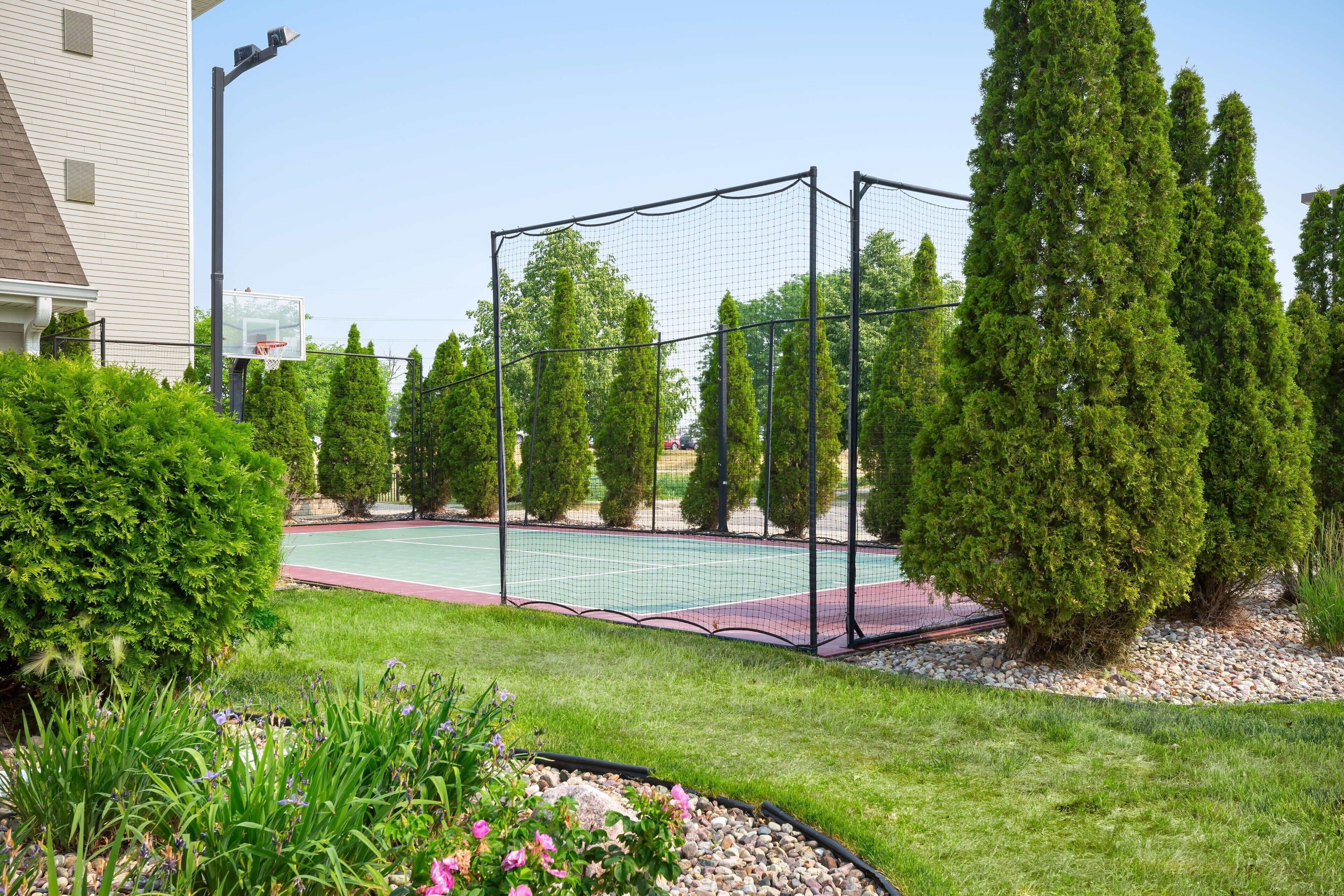 Una cancha de tenis rodeada por una cerca, árboles y un edificio.