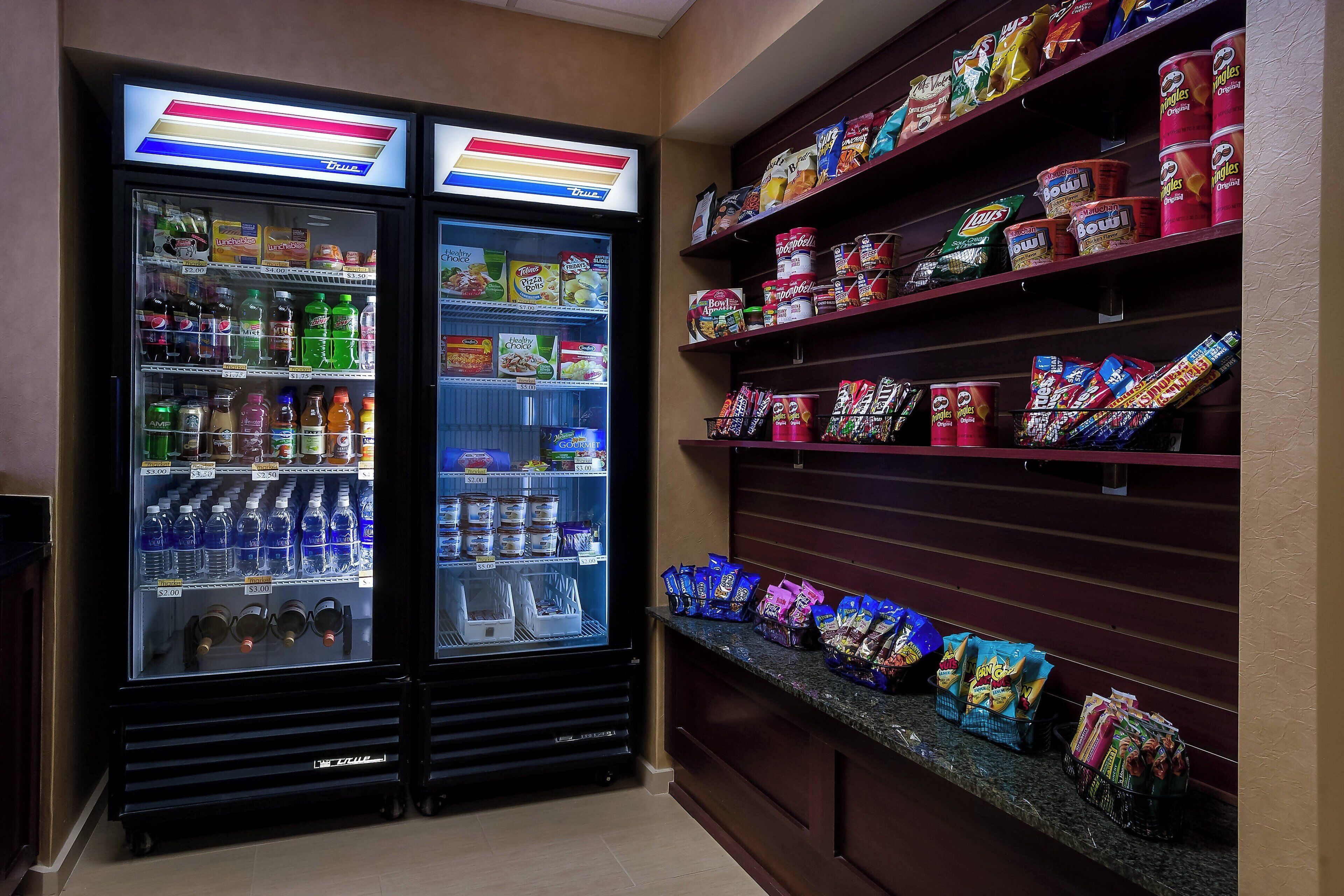 A vending area with two refrigerated drink dispensers and shelves stocked with snacks and beverages.
