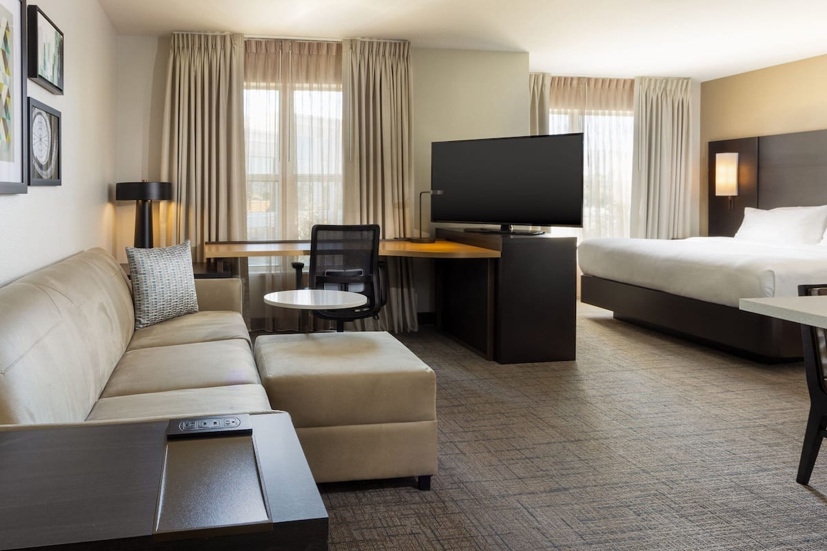A hotel room with a sofa, a desk, a television, a bed, and a window with curtains.