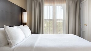 A hotel room with a large bed, a nightstand, a lamp, and a view of the outdoors through sheer curtains. - Residence Inn by Marriott Corona Riverside (Corona)