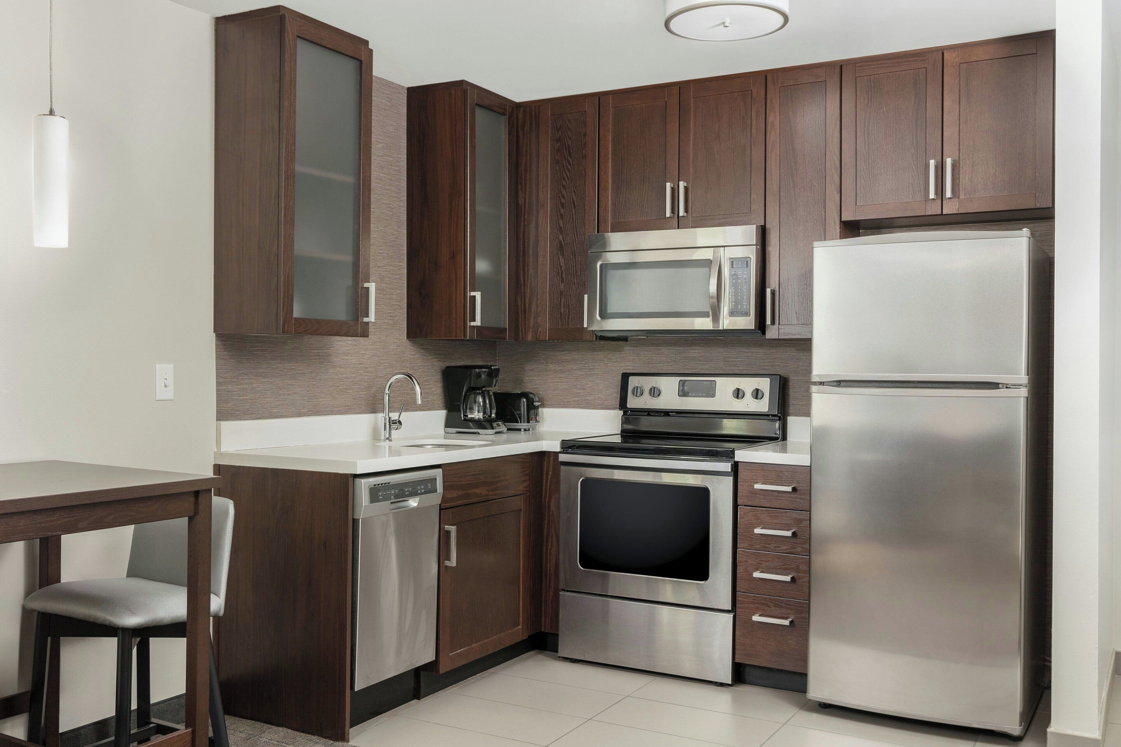 Una cocina moderna con electrodomésticos de acero inoxidable, armarios de madera y encimera blanca.