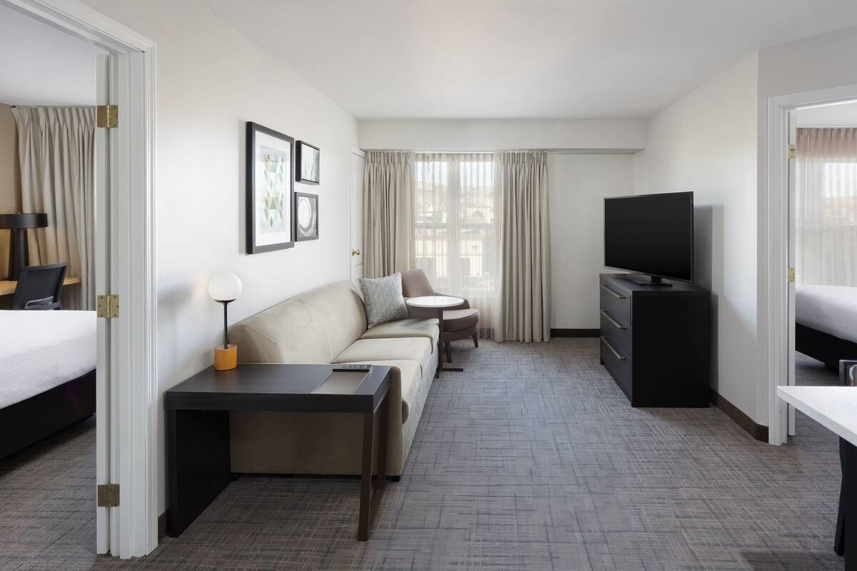 A hotel room with a bed, a sofa, a small round table, a TV, and a dresser.