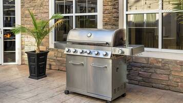 A stainless steel barbecue grill with a control panel, located on a patio with stone walls and large windows.